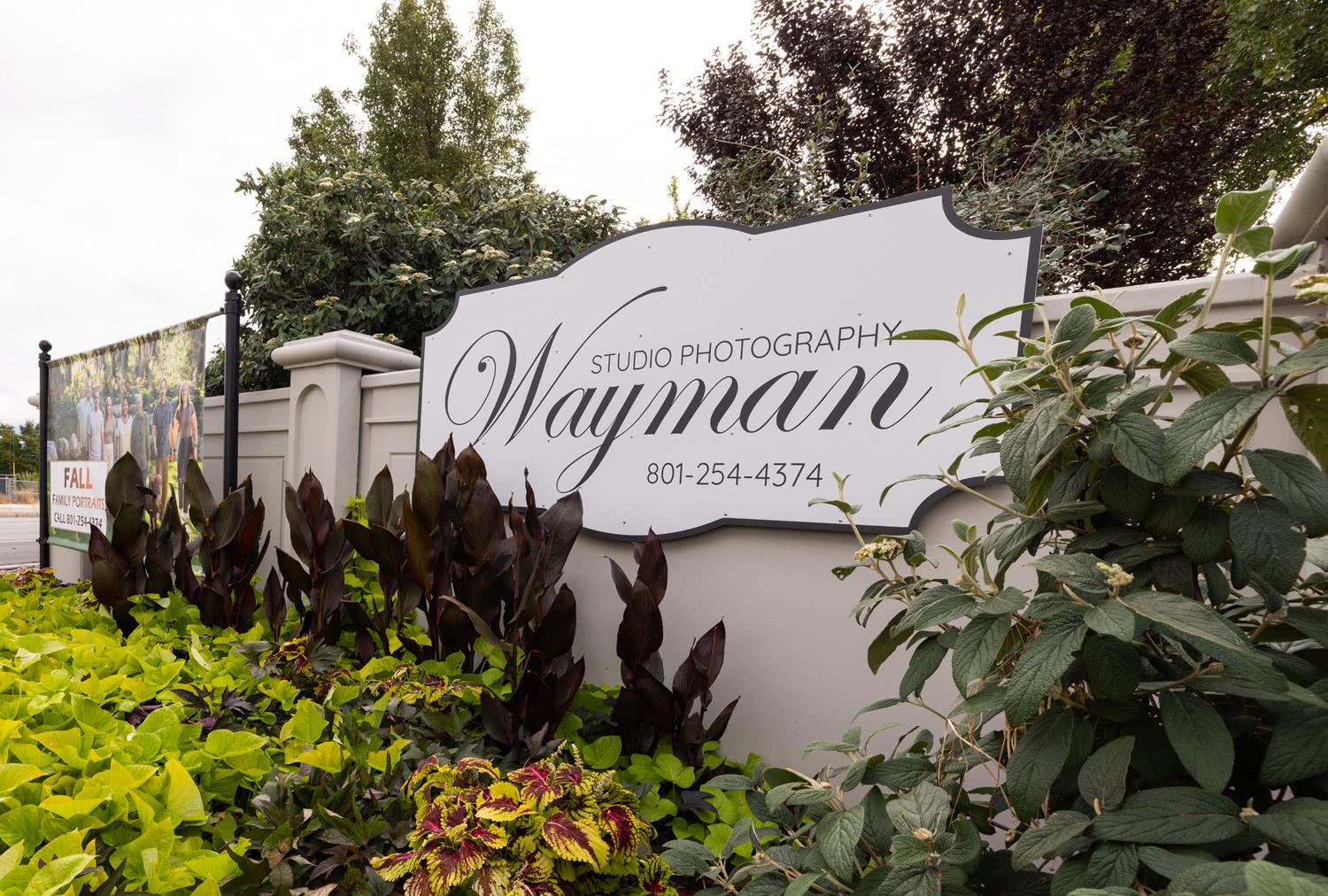 Signboard of Wayman Studio Photography, a family photo studio in Riverton, UT, surrounded by lush greenery.
