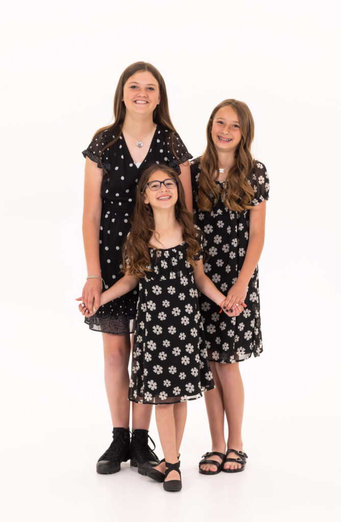 Three girls in elegant black and white dresses standing closely together, showcasing a moment of friendship and style.