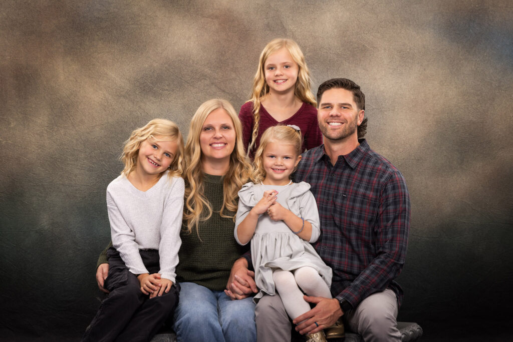 A family portrait featuring two parents and their two children, all smiling together in a warm and loving setting.